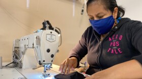 Sitting in a workshop in her garage, Leticia Mercado stitches the straps onto a black cotton mask.