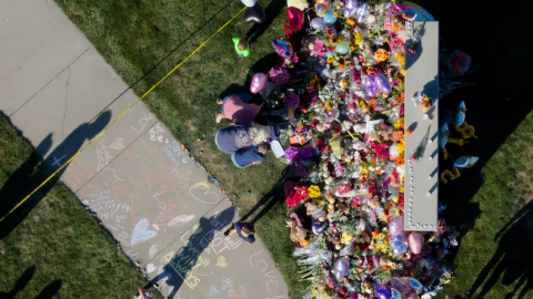 An aerial view of a memorial of flowers, balloons, and sidewalk chalk near a grassy area.
