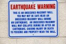 This is a picture of a sign on the side of a building that says "Earthquake Warning" and notes the masonry wall is unsecured and may not be safe to be near during an earthquake. 