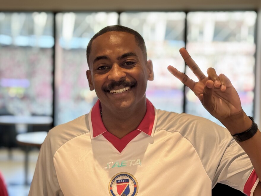 A man wearing a white shirt puts up a peace sign with his left hand. 