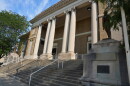 The front of a brown brick and stone building with columns, stairs and statues of soldiers.
