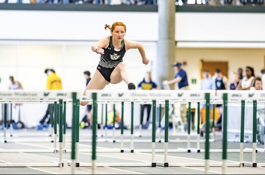 A woman jumps over a hurdle. Other hurdles surround her.