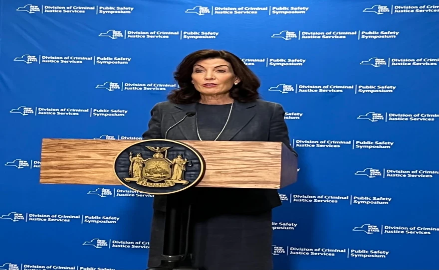 Kathy Hochul standing at a podium with a blue background