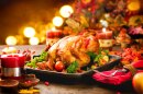 A cooked turkey on a dining table surrounded by Christmas decorations.