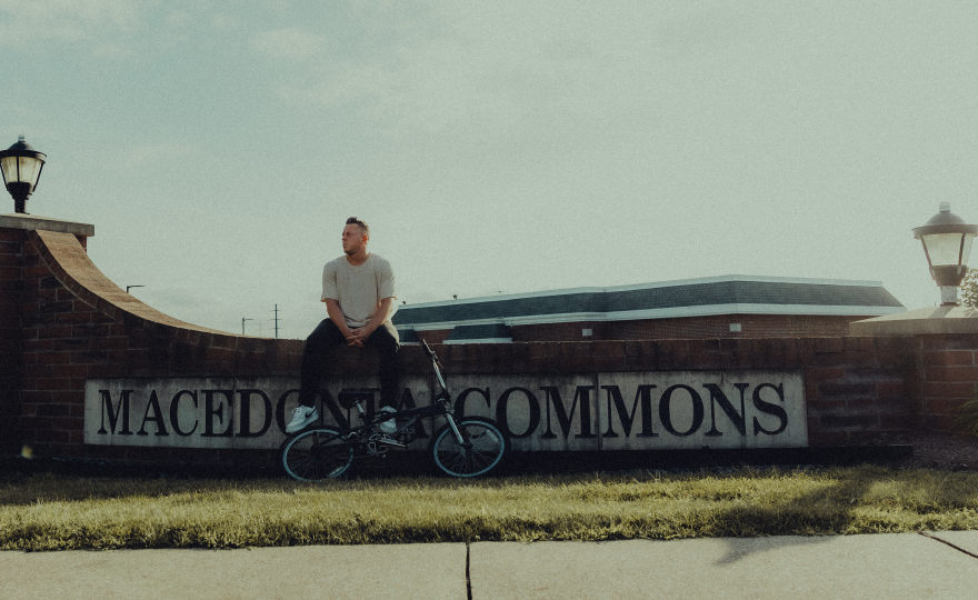Brett Zupka sits on a brick wall with the Macedonia Commons sign on it