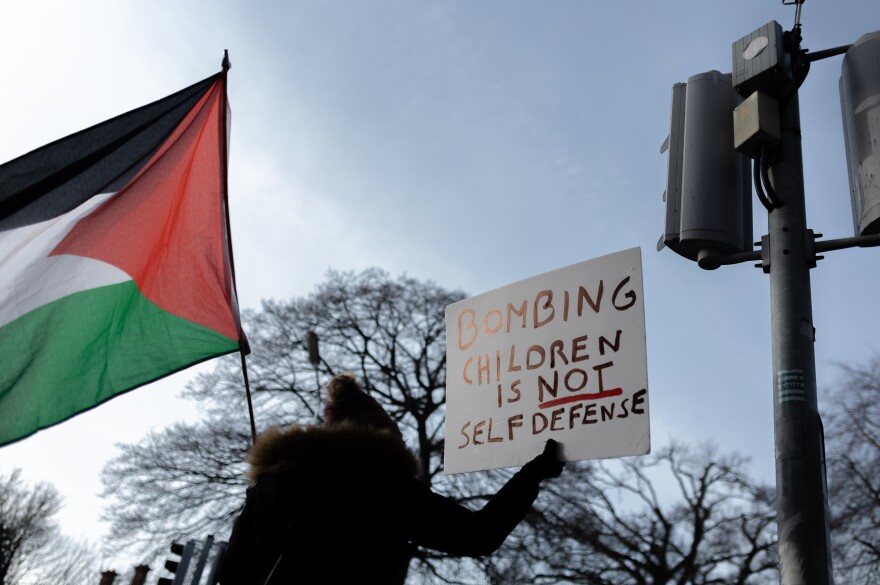 A member the group Mothers Against Genocide waves a Palestinian flag while holding a sign that reads "Bombing children is not self defense." The group met outside the U.S. Embassy in Dublin on Feb. 7.