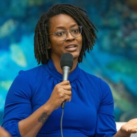 black woman in blue dress standing and talking into a microphone