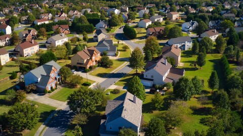 Shot using a drone during the golden hour shows an upscale suburbs with gold course, lake, houses and roof tops