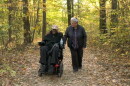 Man in wheelchair and woman walking use forest trail.
