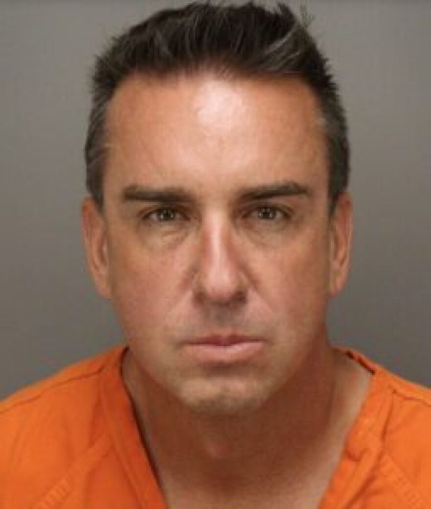 Jail mug shows a man with short brown hair and orange jumpsuit looking sternly into the camera