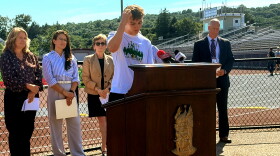 Ryan Dueker, an East Lyme High School lacrosse player and student ambassador at LAX2LIVE, a program to prevent youth suicide, spoke of the stressors that student athletes face on September 8, 2026.. He is flanked by state mental health officials. Behind him in a brown jacket is Ann Dagle, co-founder of the Brian Dagle Foundation and mother of Brian, a former student at the high school, who died by suicide when in college. The foundation runs the LAX2LIVE initiative.