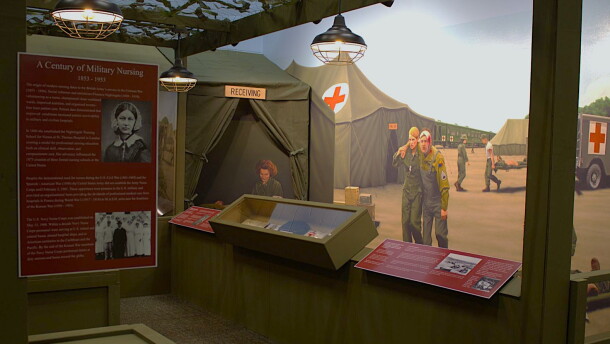 A wall mural of military nurses helping injured soldiers at a real evacuation hospital from WWII can be seen behind displays of Iowa nurses' stories and artifacts.