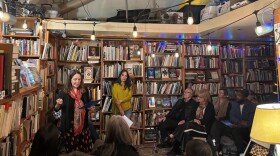 Monterey County poet laureate Marie Boucher aka Marie Butcher is reading a poem at Old Capitol Books in Monterey on Saturday, April 25. There is a lady in a yellow shirt standing beside her and a crowd of people watching to the right.