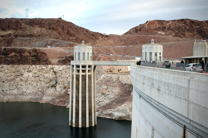 A lake with low water levels against a dam. There's a visible ring of where the water used to be much higher than it now sits.