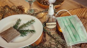 Christmas eve holiday party decorated table set with disposable medical mask and alcohol hand sanitizer bottle.