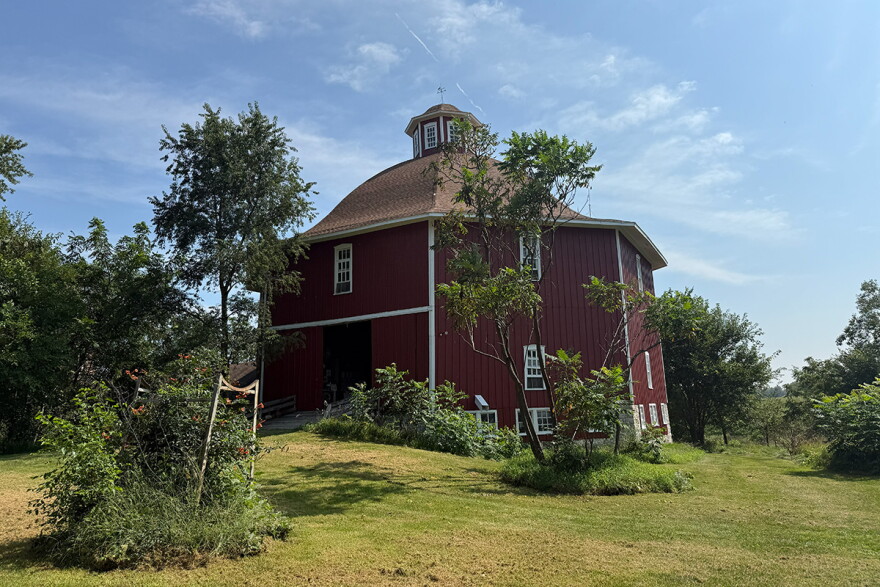 A red, octagonal barn is seen among greenery. 