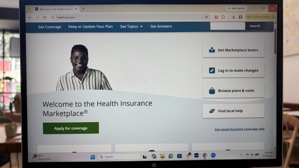 A laptop screen is open to healthcare.gov which has a button to apply for coverage.
