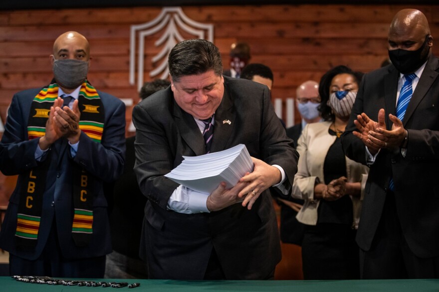 Flanked by lawmakers and supporters, Gov. JB Pritzker picks up the nearly 800-page criminal justice reform bill after signing it into law during a ceremony at Chicago State University on the South Side on Feb. 22, 2021. The legislation ended the use of cash bail in the state, a change that goes into effect on Sept. 18, 2023