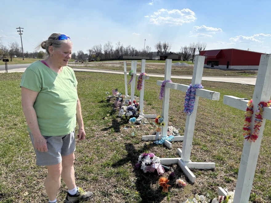 Collage artist Aleta Stone visits the white crosses put up in remembrance of those who died in the 2025 tornado. It's close to where she collected remnants for the collages that became art awards.