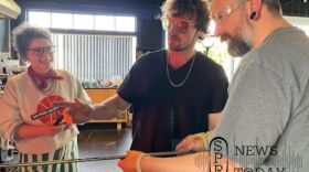 From left to right: Leah Morgan and Anthony Remick, both Tacoma glass artists, show Justin Peterson how to create a piece of glass art. The artists were commissioned to create medallions for the World Cup games, some of which will be played in Seattle, and have been involving community members in the process.