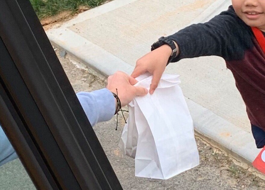 Stanly County Public Schools teacher Kristen Herlocker hands a bag lunch to a student at his bus stop.