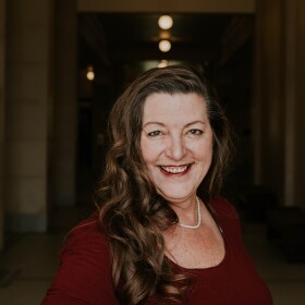 A headshot of Holly Richardson. She is wearing a red dress and smiling at the camera.