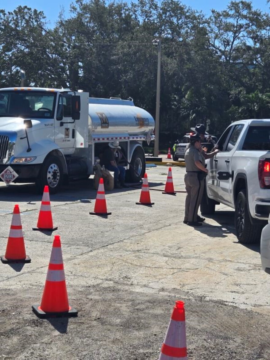 A gas tanker on the left with cones in the middle and cars to the right