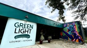 Exterior of a building says Green Light Lounge + Kitchen on a white wall with a mural of a purple cat to the right