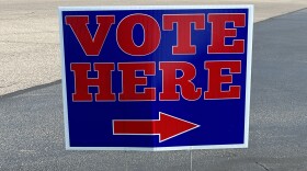 A read and blue sign that says "vote here" with an arrow.