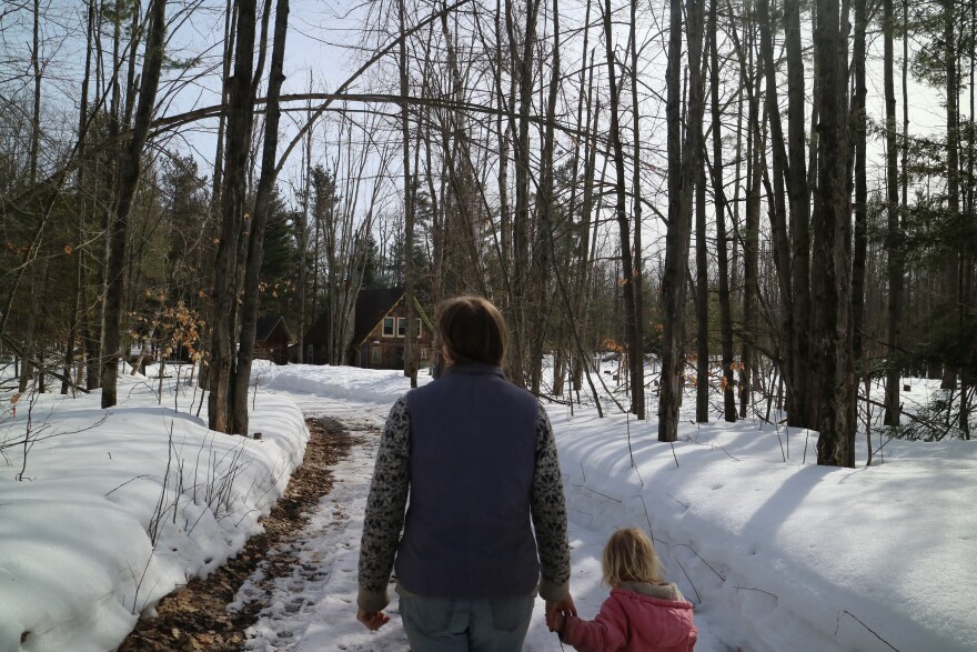 Potato farmer, Amanda Wolters holds her daughter's hand as they walk around their farm and look at damaged trees. Above them is a tree damaged so badly that it's arched over the walkway. The trails are snowy and the sky is blue. 