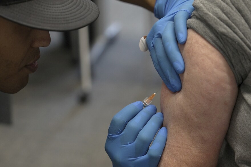 A person wearing rubber gloves holds an arm still as they prepare to inject a syringe. 