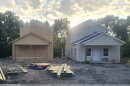 Two houses sit at a construction site. The one on the right is almost finished, while the one on the left still needs exterior paneling and a roof.