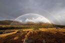 Two rainbows stand over a mountain where wildfire smoke rises.