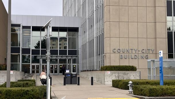 People walk in and out of a tall tan and glass building with a sign "County-City Building" on the exterior.