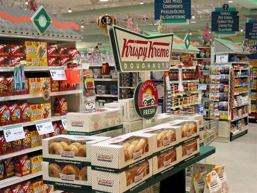 A supermarket display of Krispy Kreme Doughnuts and other junk food.