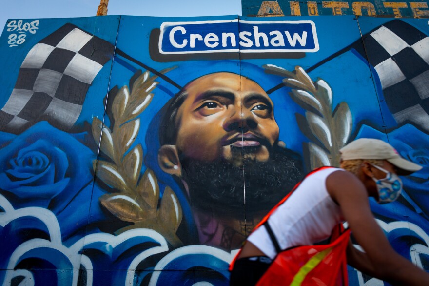 Los Angeles, CA � Residents pass by a mural on Slauson Avenue in Crenshaw Dec. 5, 2020. In the wake of Nipsey Hussle's March 2019 death, many murals of the beloved Los Angeles musician were painted in the Hyde Park neighborhood near his Marathon clothing store. The store and a large Nipsey mural in its alleyway are now fenced off but other nearby murals continue to draw local and visiting fans.