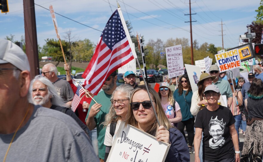 A large crowd of protesters stands along a busy street in Medford, Oregon, holding handmade signs and American flags during a “No Kings” demonstration.