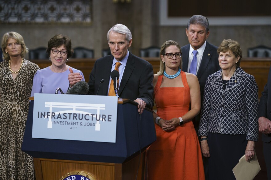 FILE - In this July 28, 2021, file photo the bipartisan group of Senate negotiators, from left, Sen. Lisa Murkowski, R-Alaska, Sen. Susan Collins, R-Maine, Sen. Rob Portman, R-Ohio, Sen. Kyrsten Sinema, D-Ariz., Sen. Joe Manchin, D-W.Va., and Sen. Jeanne Shaheen, D-N.H., speak to reporters just after a vote to start work on a nearly $1 trillion bipartisan infrastructure package, at the Capitol in Washington. Senators are convening for a rare weekend session on the bipartisan infrastructure bill as they edge toward a vote, Saturday, Aug. 7, 2021. (AP Photo/J. Scott Applewhite, File)