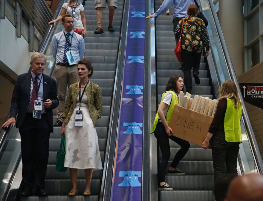 Convention staff carry a box of signs to the upper levels of the Wells Fargo Center to hand out to the crowd.
