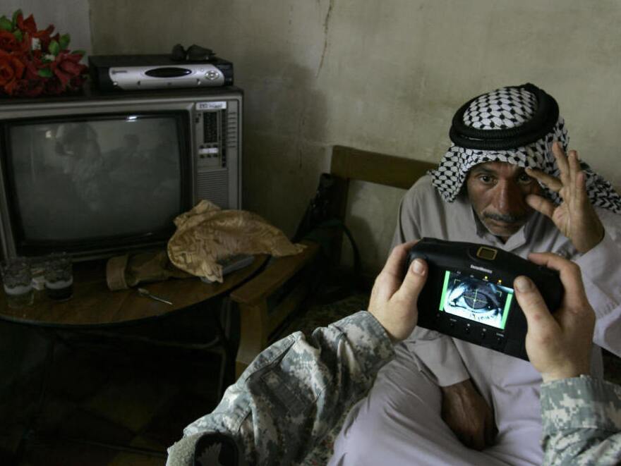 An Iraqi man stretches his eye as a U.S. soldier scans his iris using a biometrics digital system camera during an enlistment program session to join the Sahwa group in Mahmudiyah, in 2008.&nbsp;