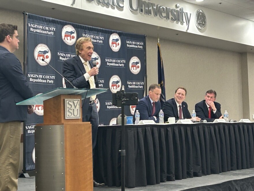 Republican gubernatorial candidate Perry Johnson (center standing) speaks as debate moderator Dave Bondy (Left), and fellow candidates Tom Leonard, Aric Nesbitt and Ralph Rebandt (L-R) listen at the Michigan Republican Gubernatorial Forum on March 5th, 2026.