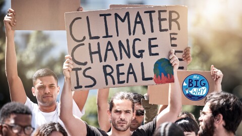 A stock photo shows a group of protesters holding up signs made of cardboard. A man in the middle of the frame holds a sign above his head that says "climate change is real", with a picture of a burning globe below it. 