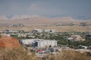 A city of white buildings is shown in the distance, sitting between red rock canyons and desert. 