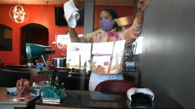 A younger worker at a nail salon cleans a plexiglass shield being used to prevent the spread of COVID-19.