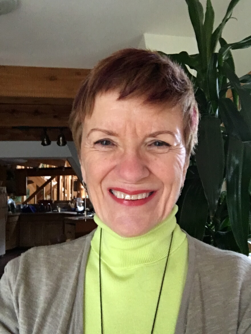 A woman wearing a neon green turtleneck with a large green plant behind her.