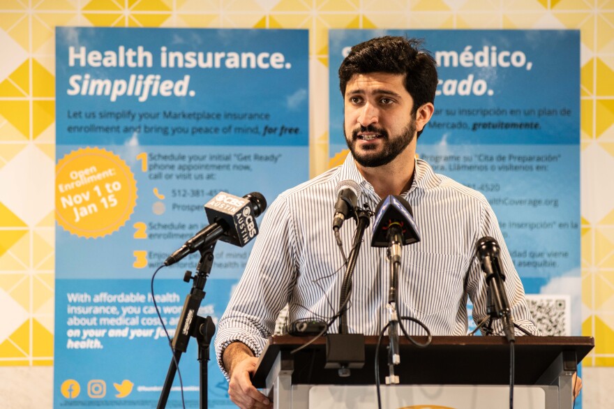 Greg Casar at a podium in front of signs to enroll in the Affordable Care Act's insurance plan. 