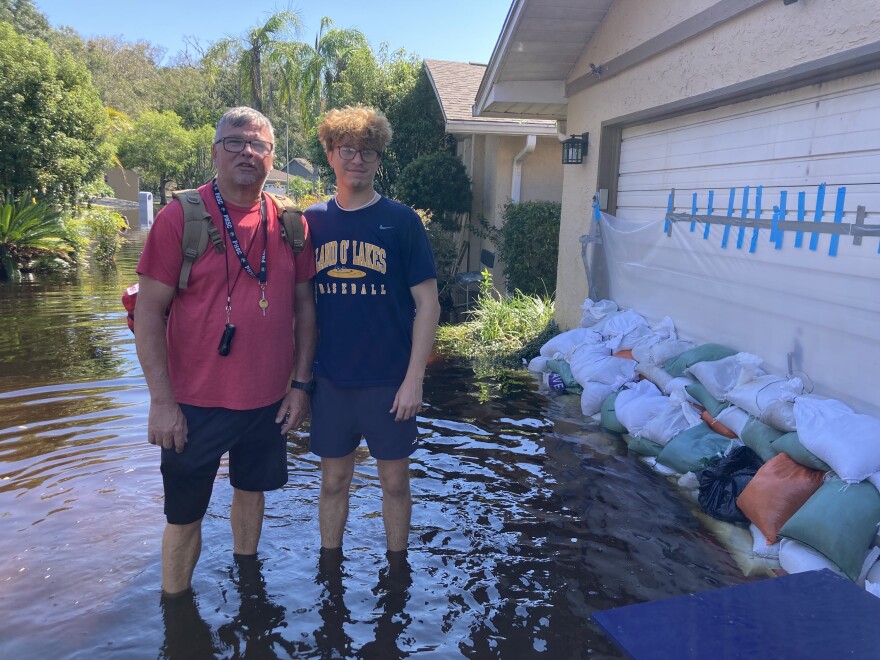 Two people stand next to their flooded street