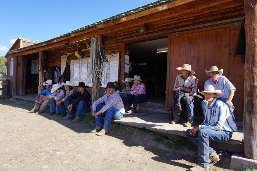 About a dozen young people sit on a wooden porch in jeans and cowboy hats.