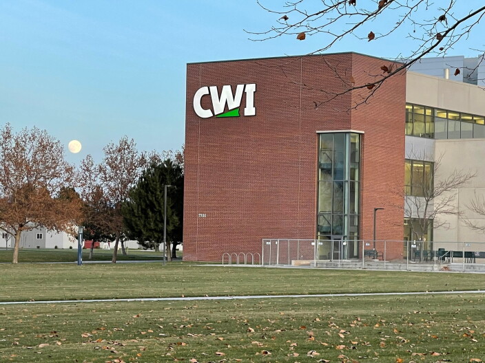 A red brick building with the large letters "CWI" on the side of it. There is a grass lawn in front of the building and some metal wire fencing.