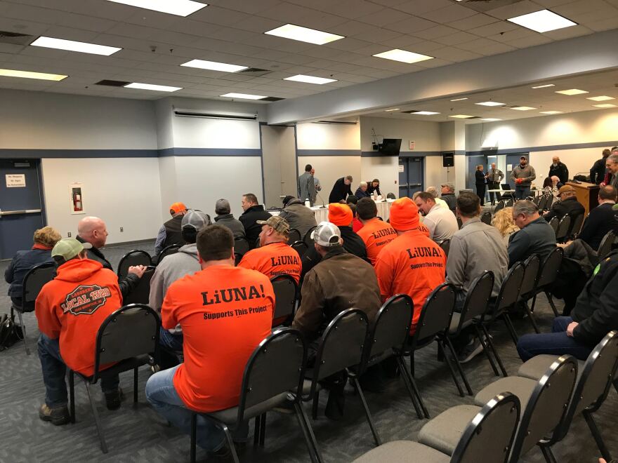 Rows of men in orange union t-shirts sit in a large meeting room filled with chairs.